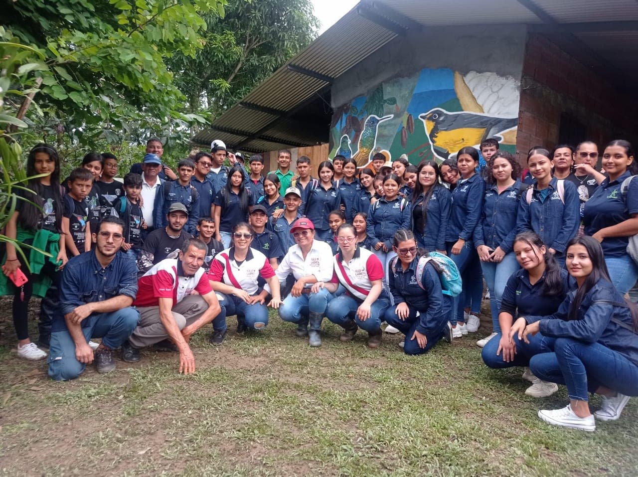 Large school group posing with the farm team in front of the bird mural